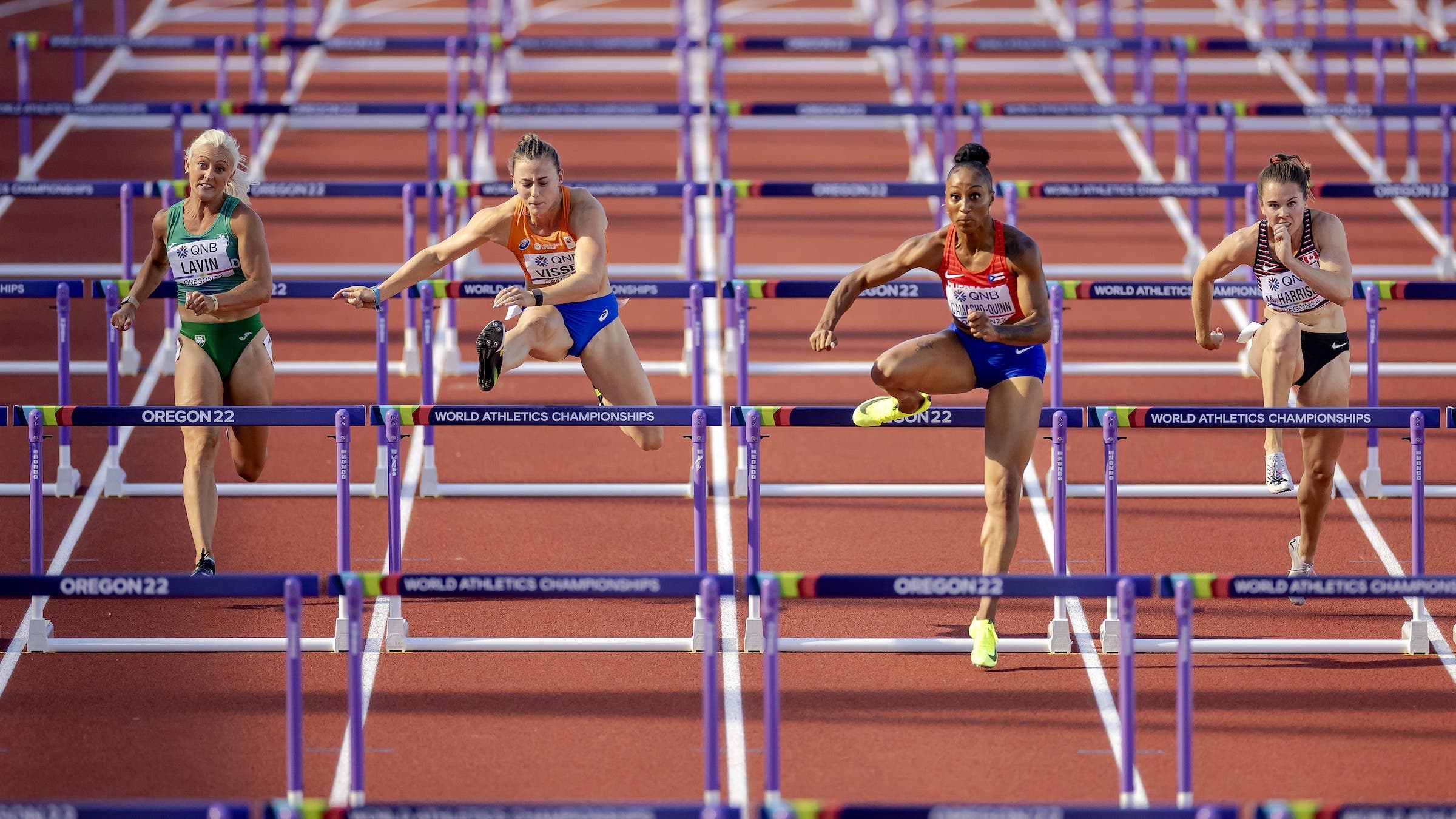 Four women take on hurdles on a red track 