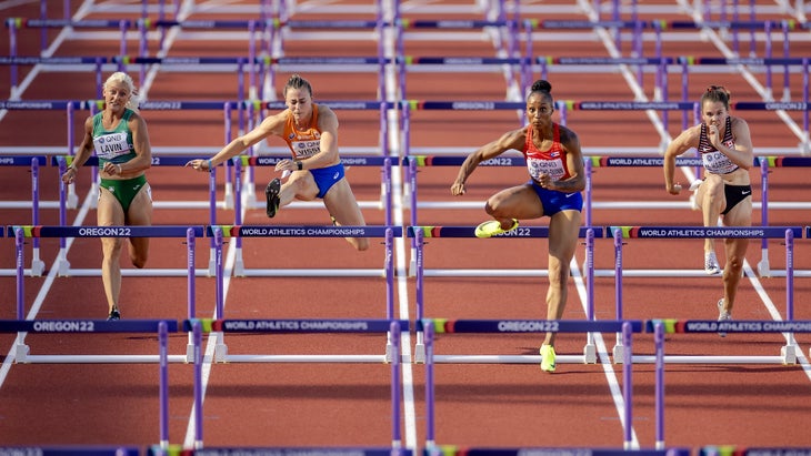 Four women take on hurdles on a red track 