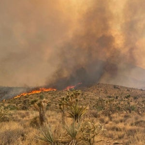Fire and smoke billows over a hill formation in a desert landscape.