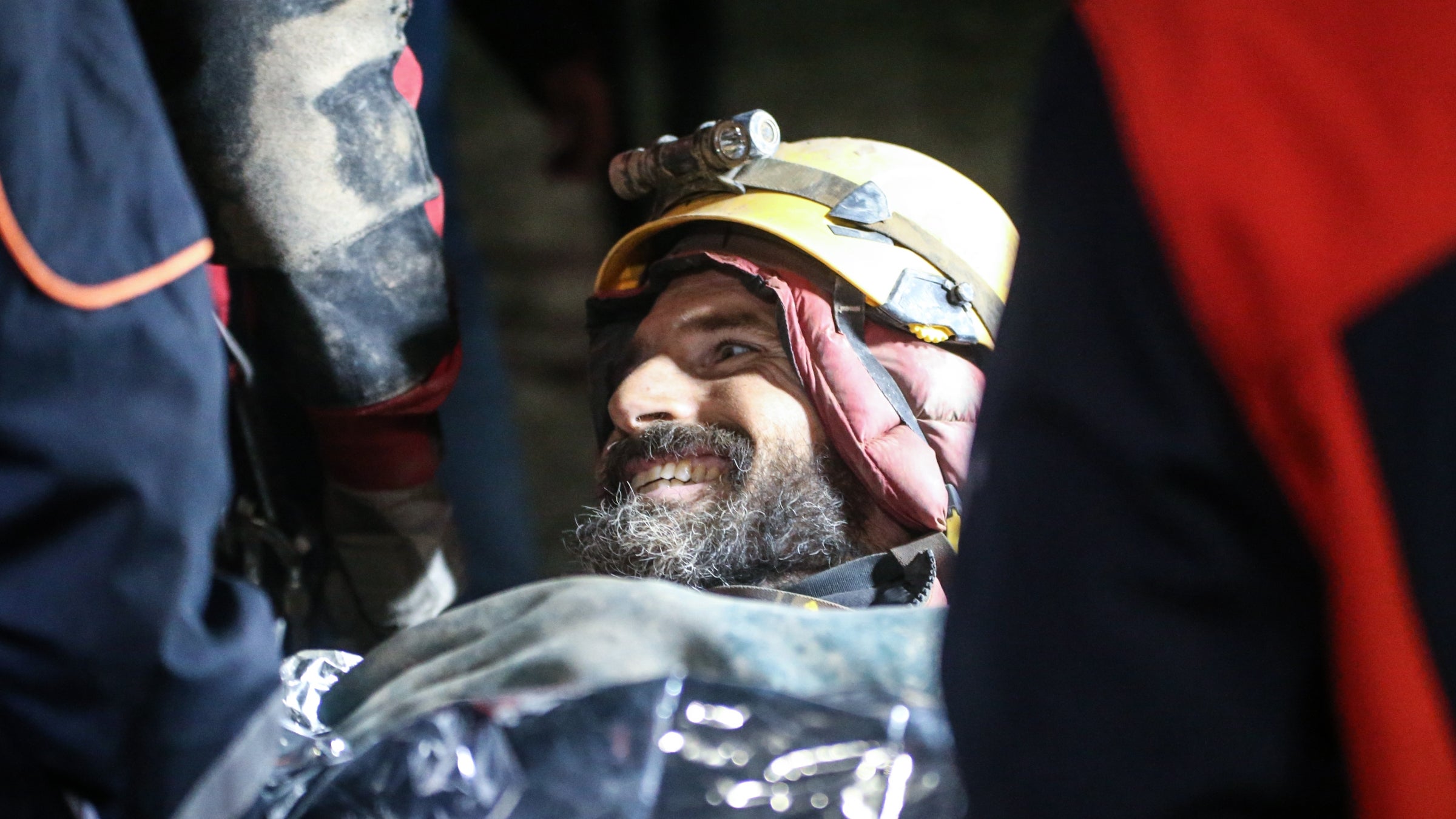 A man wearing a hard hat and winter coat smiles from a stretcher.