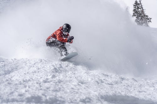 Woman snowboarding out of a drift of snow