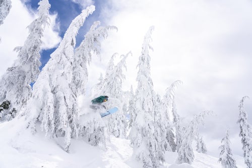 Man doing a jump through the trees on a snowboards