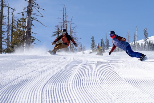 Three snowboarders carving a groomer