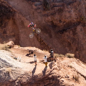 A mountain biker jumps in the desert, with three spectators below him.
