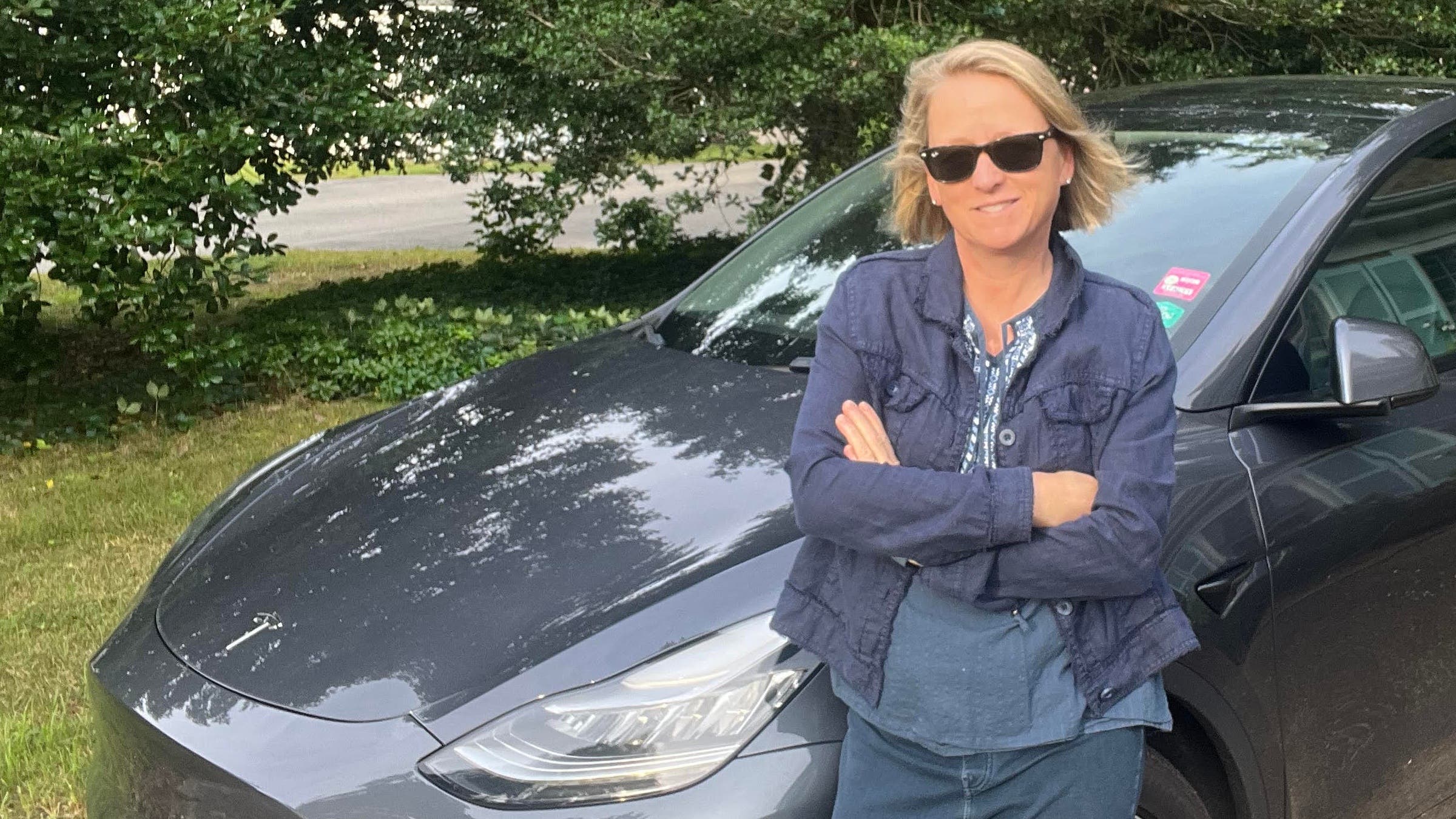 The author proudly leans up against her blue Tesla electric car after weighing the environmental pros and cons of keeping her old car.