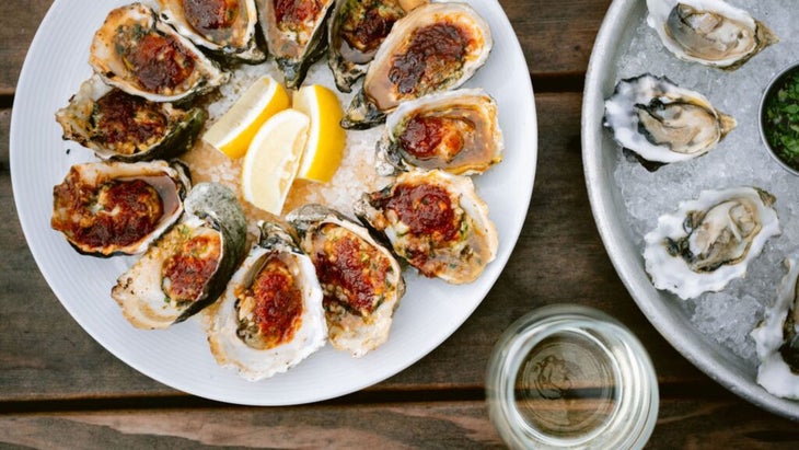 A platter of barbecue oysters aside a round tray of plain oysters over ice