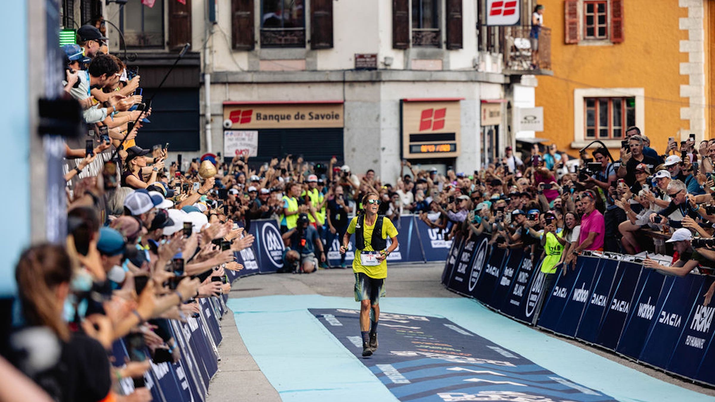 a woman in a yellow shirt finishes the race to a large crowd