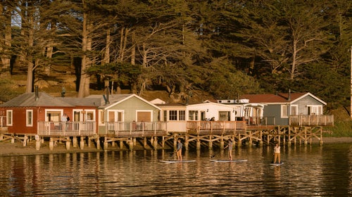 An exterior view of the five waterfront cottages of Nick's Cove, with three stand-up paddle boarders in the foreground