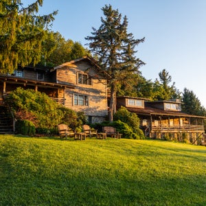 The exterior of The Swag, a wooden hotel set atop a lush lawn, with Adirondack chairs out front