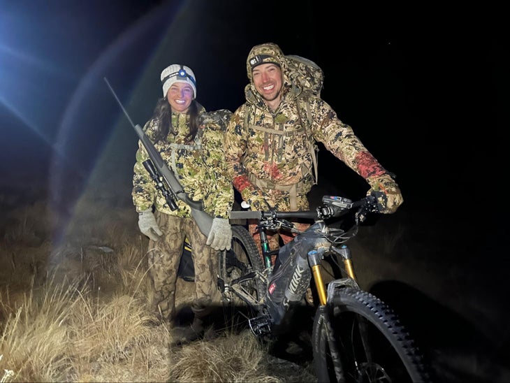 A couple in camouflage standing by an e-bike at night