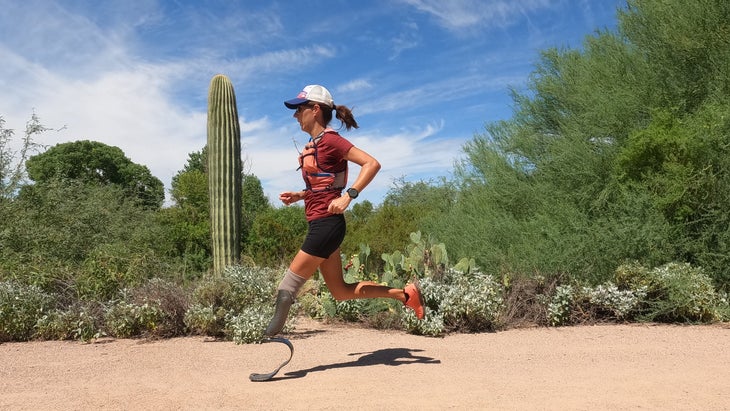An adaptive athlete in a red shirt runs in a desert landscape
