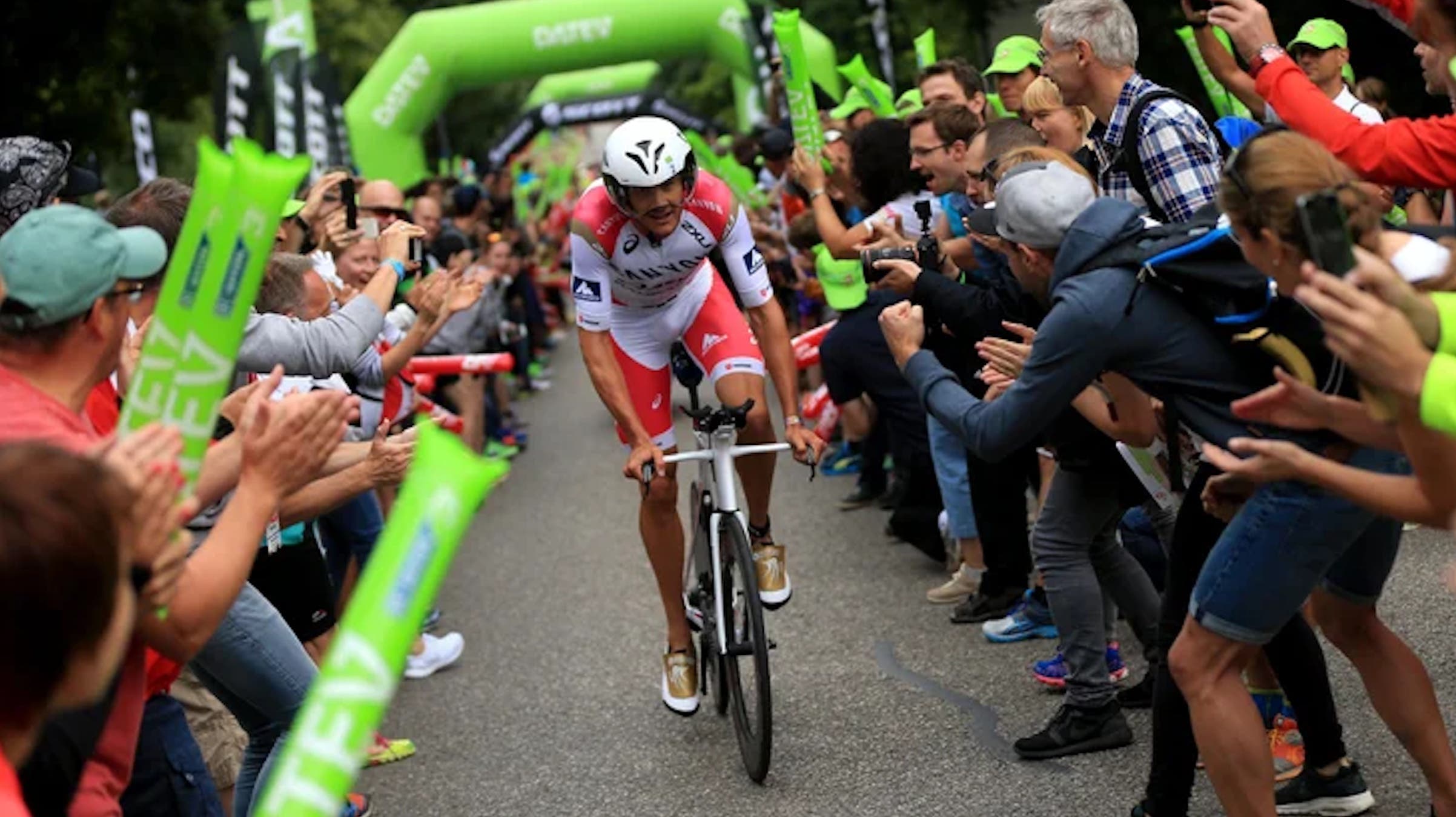 An ironman cycles through a tunnel of green and spectators