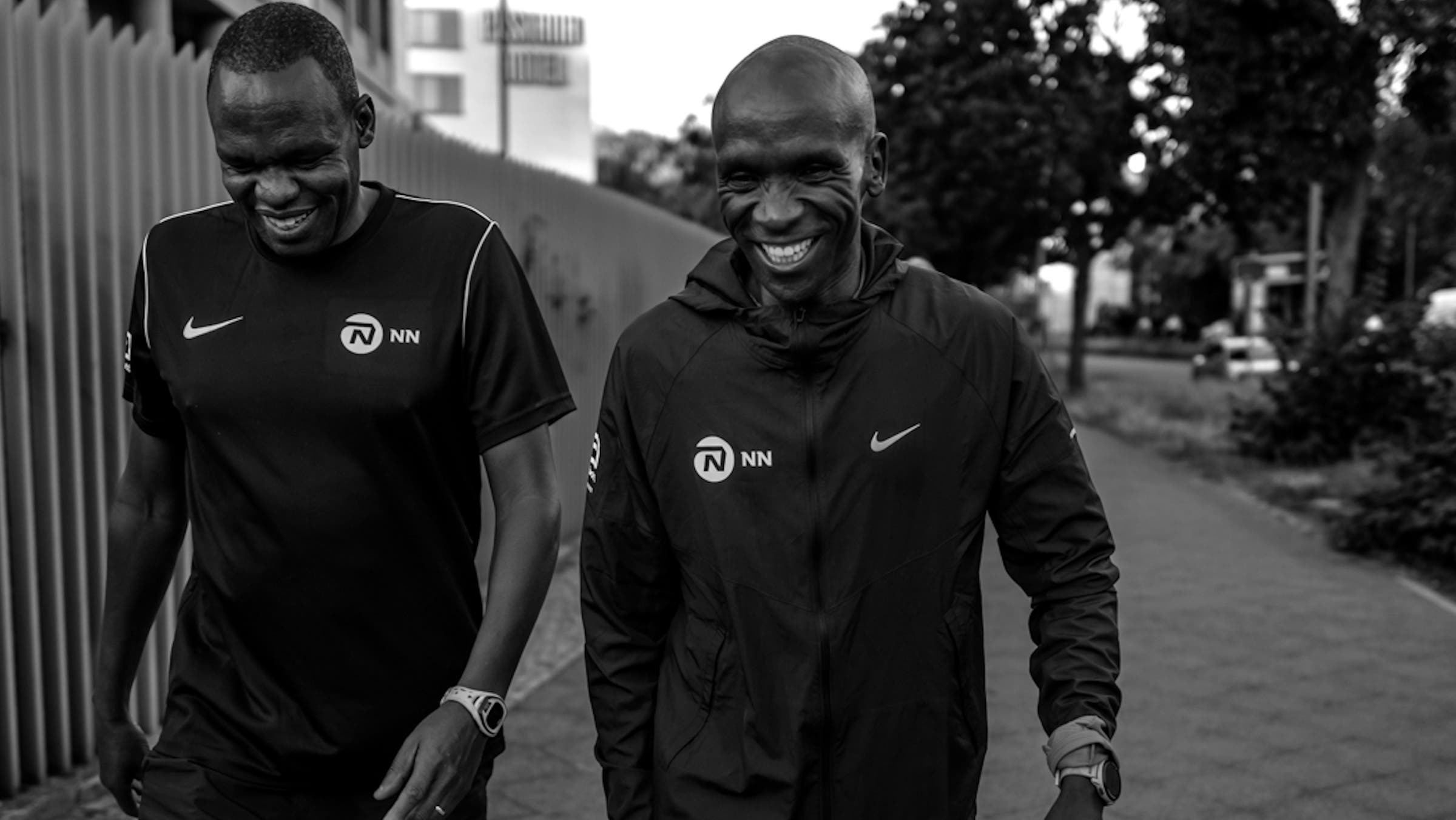 Two men in a black and white photo walk a street in Berlin, laughing