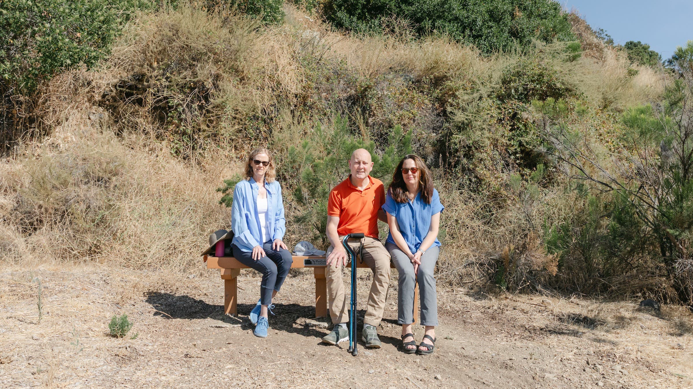 three people sit on a bench in a park