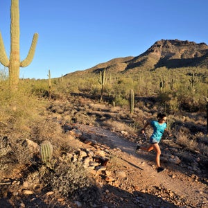 Woman runs in a blue shirt in the desert with a cactus behind her