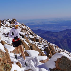 A man in white runs up a trail in the snow