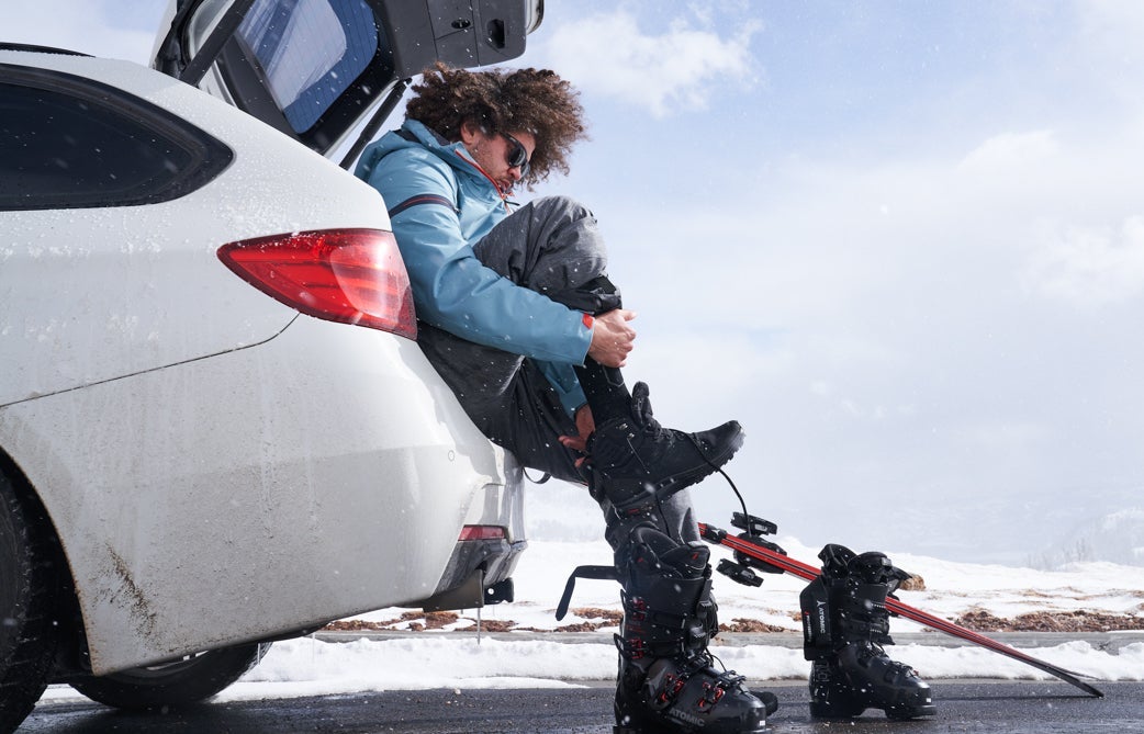 Man sitting in the trunk of a white car putting on ski boots.
