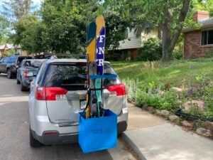Blue Chuck Bucket ski carry system loaded with multiple pairs of skis and mounted on grey minivan on a neighborhood street