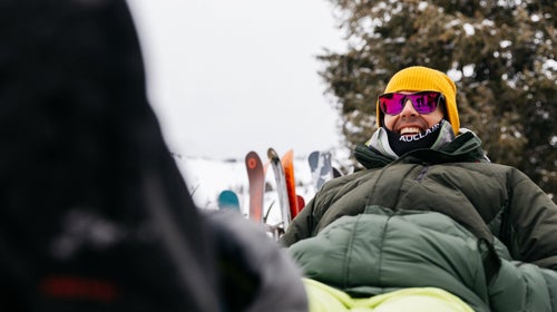 Man wearing ski clothing sitting on chair with feet propped up