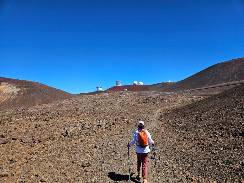 Woman hiking near the summit of Mauna Kea volcano with observatories in the background.