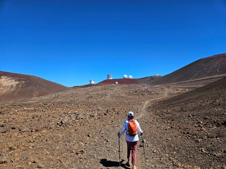 Woman hiking near the summit of Mauna Kea volcano with observatories in the background.