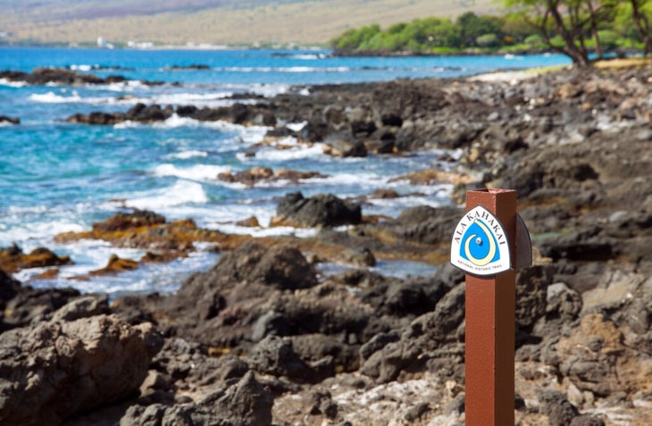 Sign post for the Ala Kahakai National Historic Trail with volcanic rock and ocean