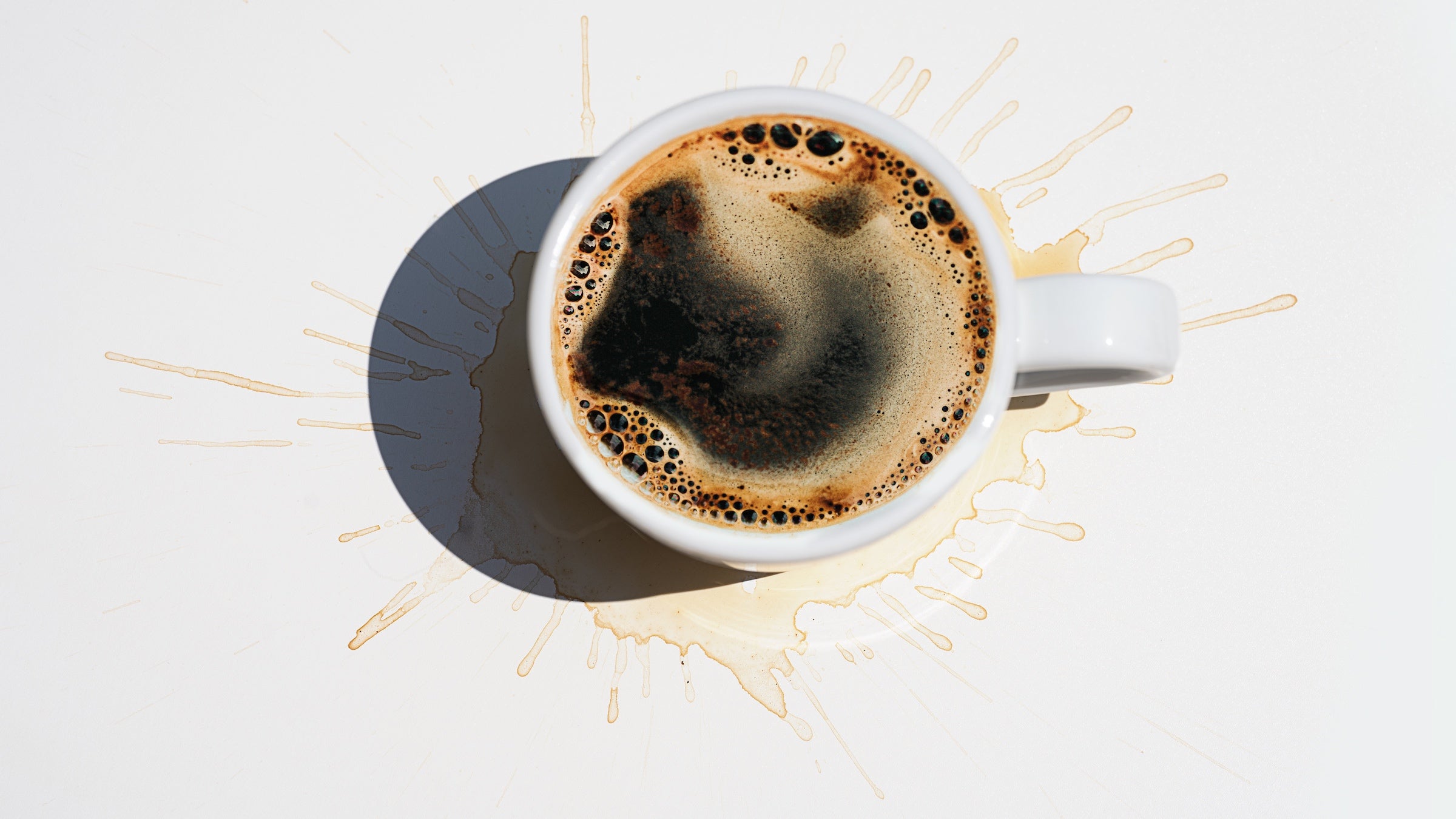 Aromatic morning coffee in a white cup and splash marks from spilled coffee on white color background.