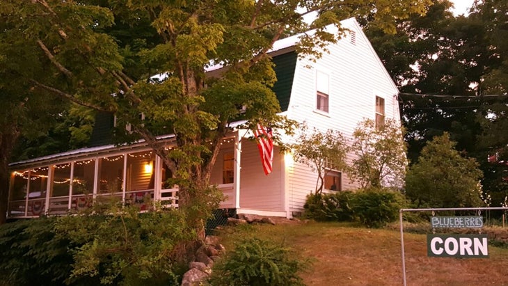 The whitewashed Farmstead bed-and-breakfast, with an American flag hanging outside and a front porch visible