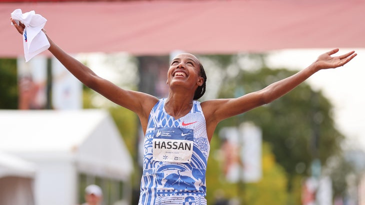 A woman in a blue and white shirt celebrates winning a marathon