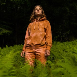 A woman wears an orange tracksuit in a bed of ferns.