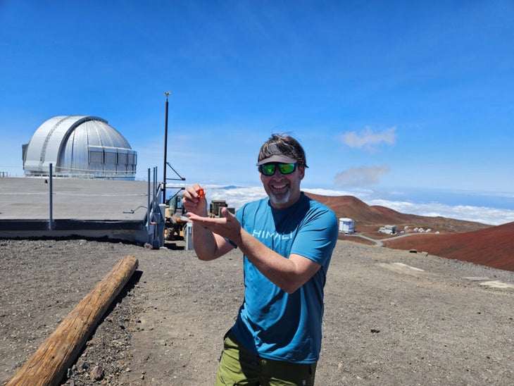 man holding a small rubber monster on the summit of Mauna Kea in Hawaii