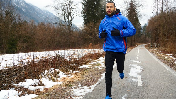 Man in sports clothing running in winter. Snow on road and fog in the park.