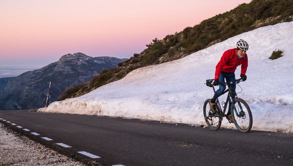 An older athlete in top form is pedalling uphill as the sun starts to set.