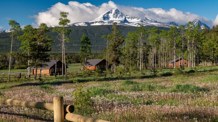 A field with tall pines and three log cabins, with a snowcapped peak in the background, set the scene at British Columbia’s Nemiah Valley Lodge