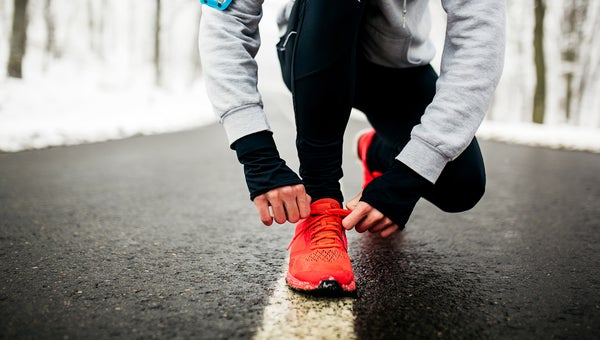 Young male runner preparing his sneakers for running. Tying shoelaces on the road.