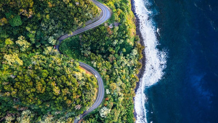 An aerial view of the serpentine Road to Hana on Maui, next to a beautiful dark-blue swath of sea