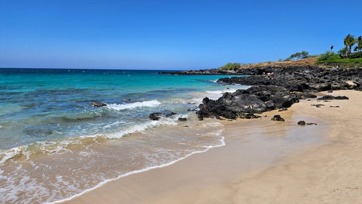 White sand beach with blue sky and rocky outcrop in Hawaii