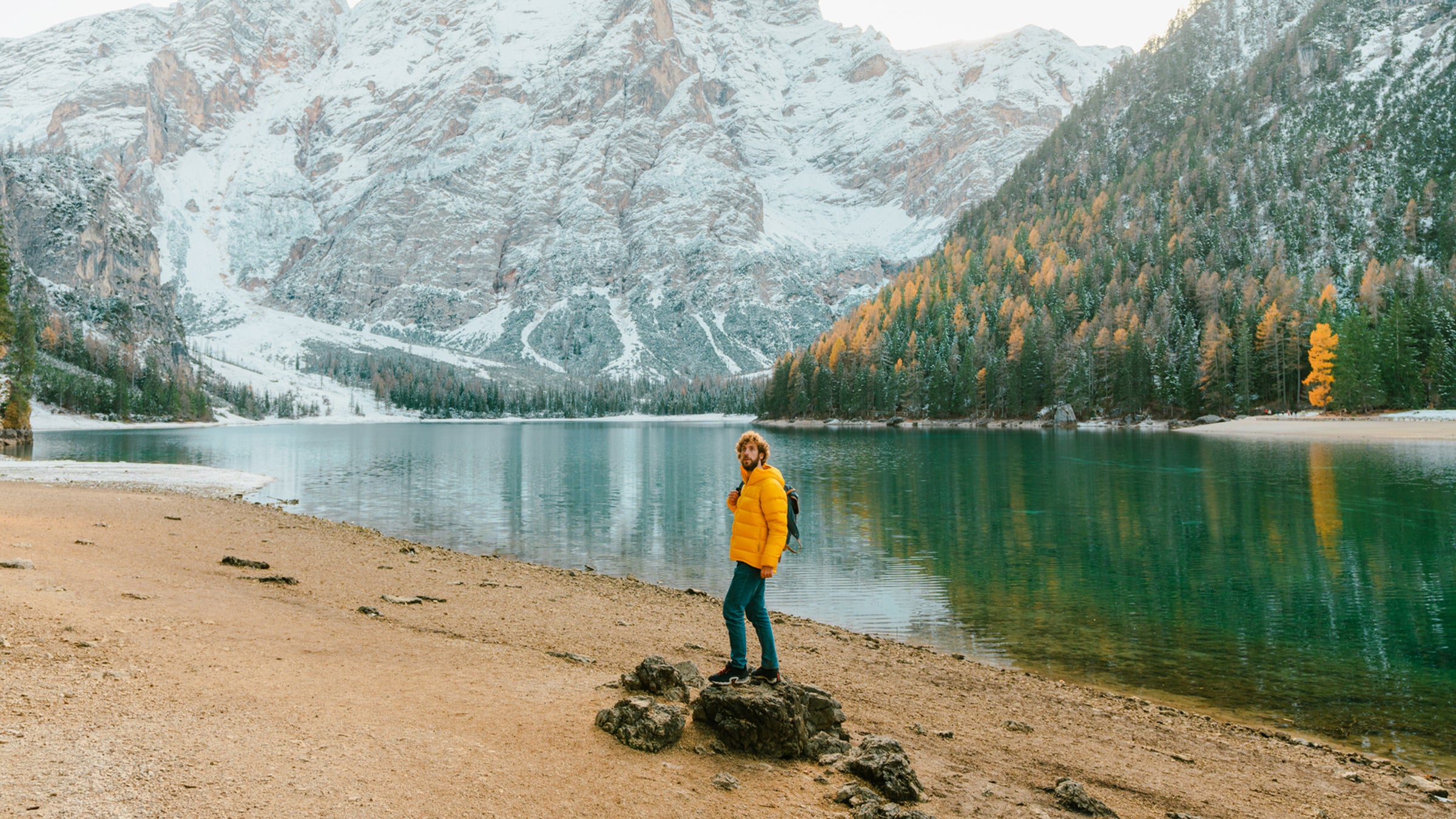 man in yellow padded jacket standing on the background of Lago di Braies lake in Dolomites, Italy.