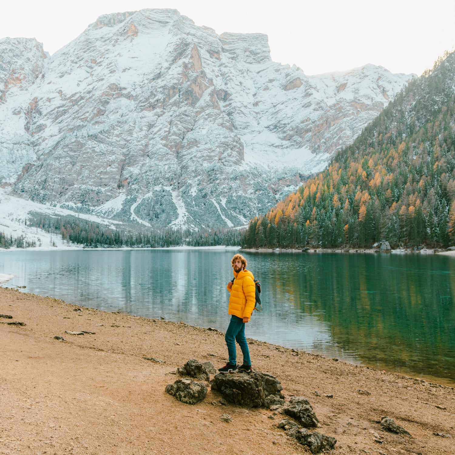 man in yellow padded jacket standing on the background of Lago di Braies lake in Dolomites, Italy.