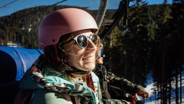 Portrait of a happy woman sitting on ski lift lift wearing sunglasses and helmet