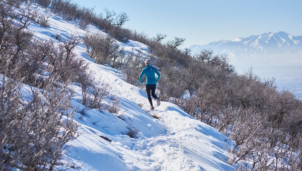 Young Woman trail running on a mountain during the spring. Spots of snow remain on trail.