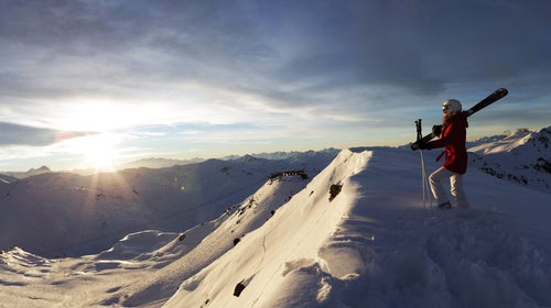 Sun breaks through clouds as skier looks on in the backcountry.