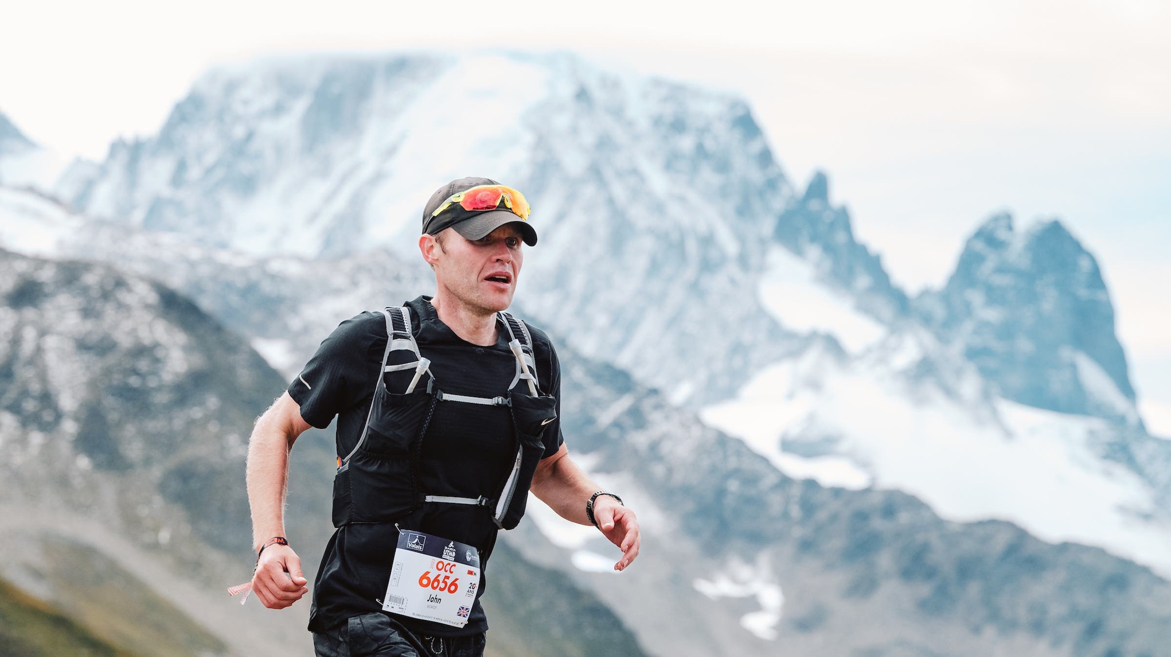 A man runs in the Alps with a pack and black shirt