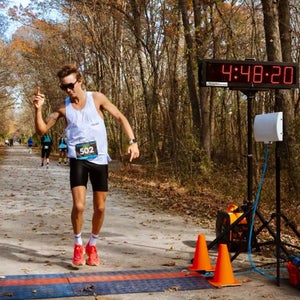 A man in a white shirt raises an arm after finishing a race