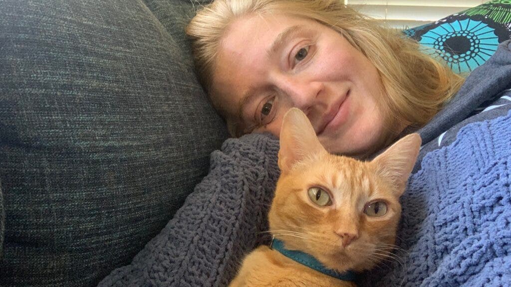 The author on a couch, nestled with an orange cat