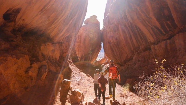 A father and his two sons walking between massive boulders within Arches National Park's Fiery Furnace