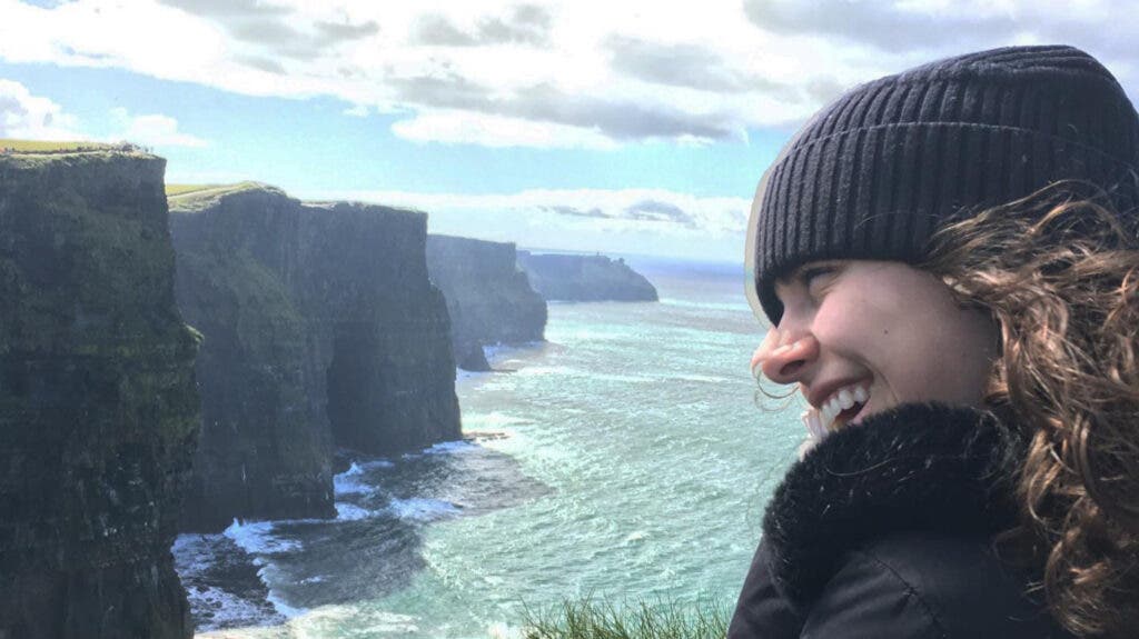 A profile head shot of the author overlooking flat-top cliffs and an icy-blue ocean below