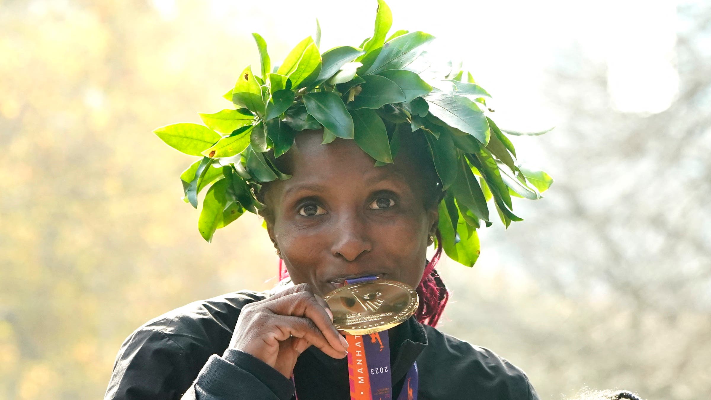 A woman kisses a medal with a green laurel on her head.