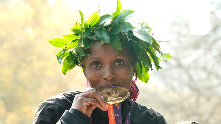 A woman kisses a medal with a green laurel on her head. 