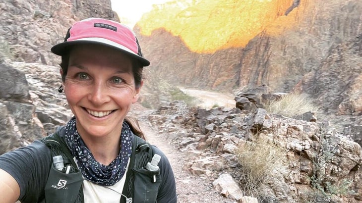 The author, wearing a cap and a trail-running vest, shooing a photo of herself in the depths of the Grand Canyon, with a sliver of the Colorado River visible in the background